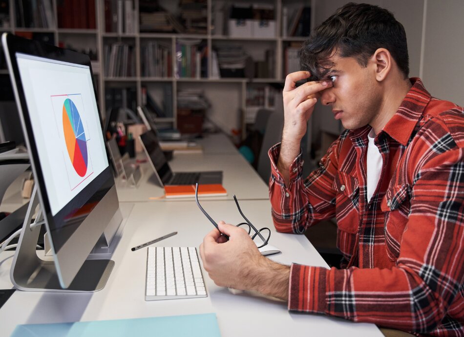 Young man looking at computer screen glasses off and rubbing eyes