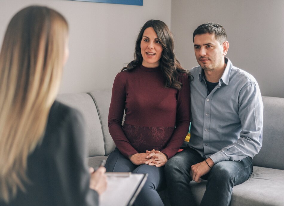 Young couple sit closely on couch talking to counsellor