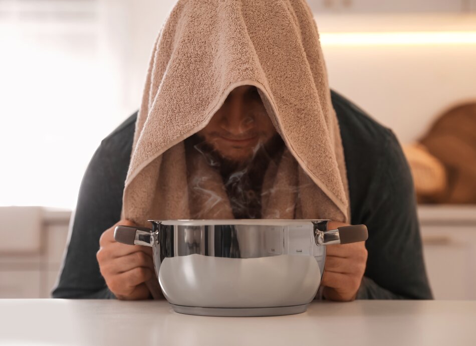 Man with towel over head inhaling steam