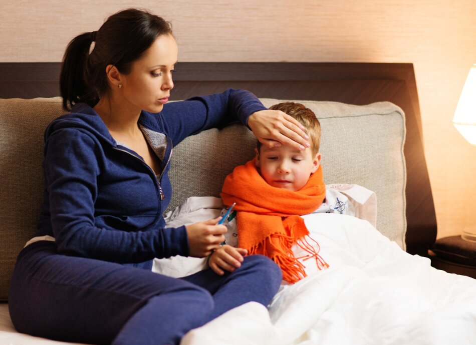 Mother checks temperature & puts hand on sick boy's forehead