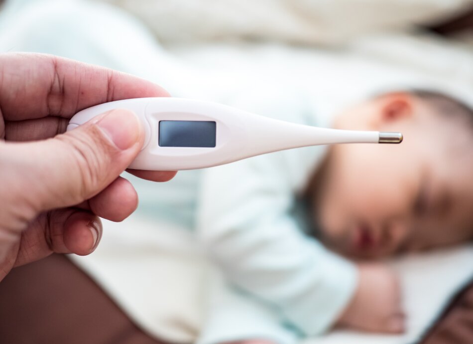 Closeup on thermometer with sleeping baby in background