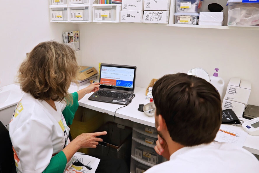 Health professional and patient in consultation room looking at influenza vaccine in adults page on computer 