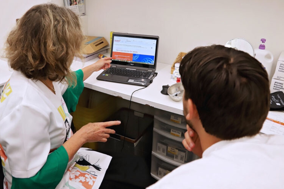 Health professional and patient in consultation room looking at vaccine page on computer 