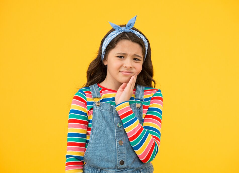 Girl with headscarf grimaces with sore tooth and touches jaw 