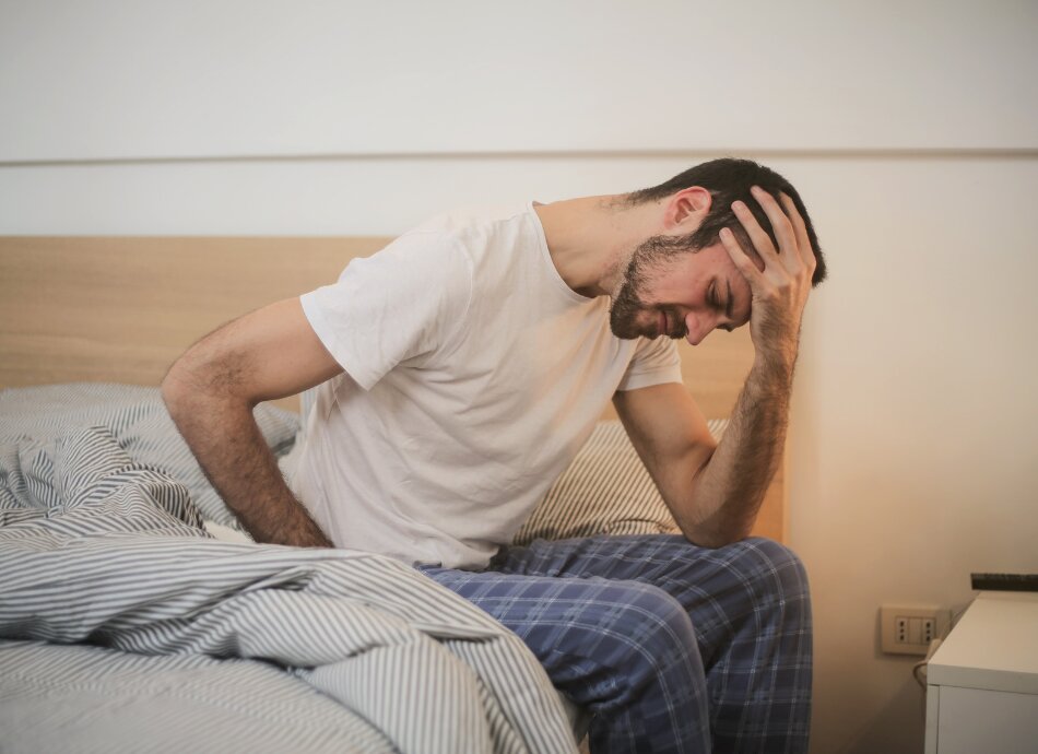 Man sitting on side of bed looking unwell & tired