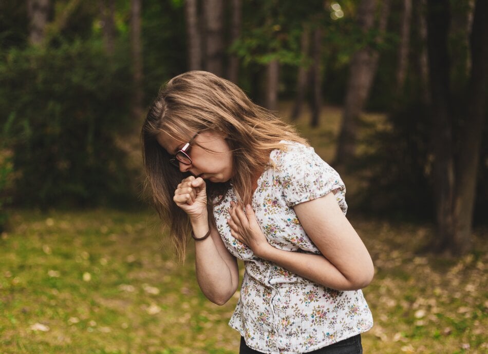 Young woman outdoors experiences pain in chest when coughing 