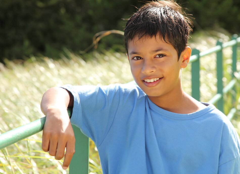 Boy leaning on fence railing in sunshine