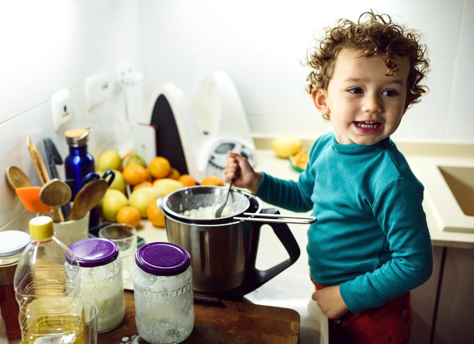 Young child stirring food in a pot on the bench