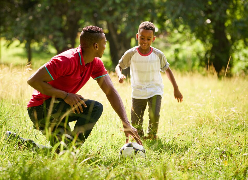 Man with young boy kicking football