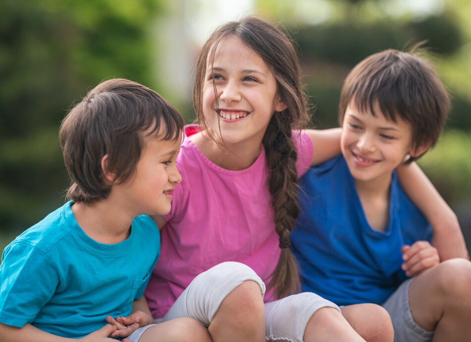 Three affectionate siblings sitting closely together outside