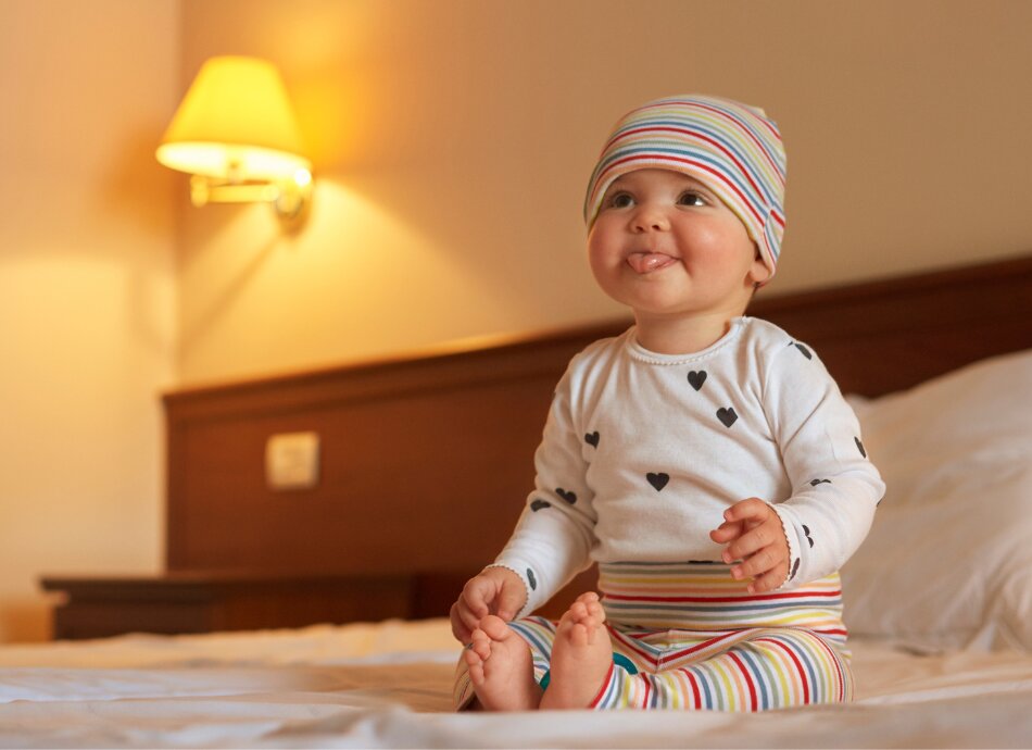 Toddler sitting on bed sticking tongue out 