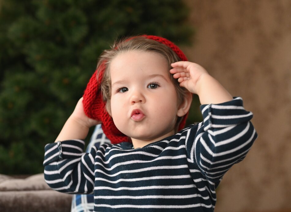 1-year old child in striped top trying to put on a hat