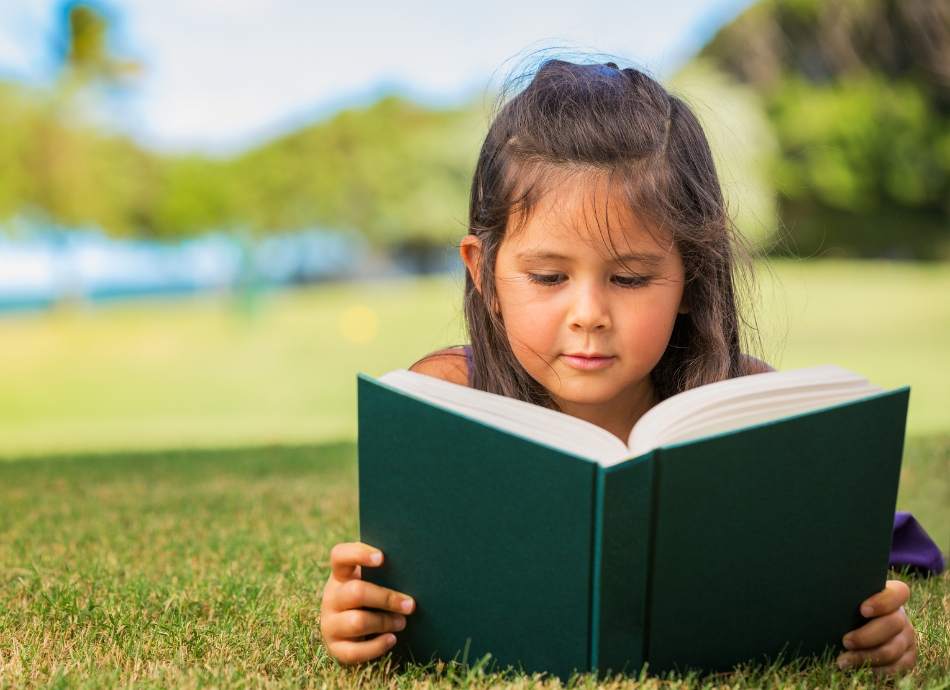 Young girl lying on tummy reading a book