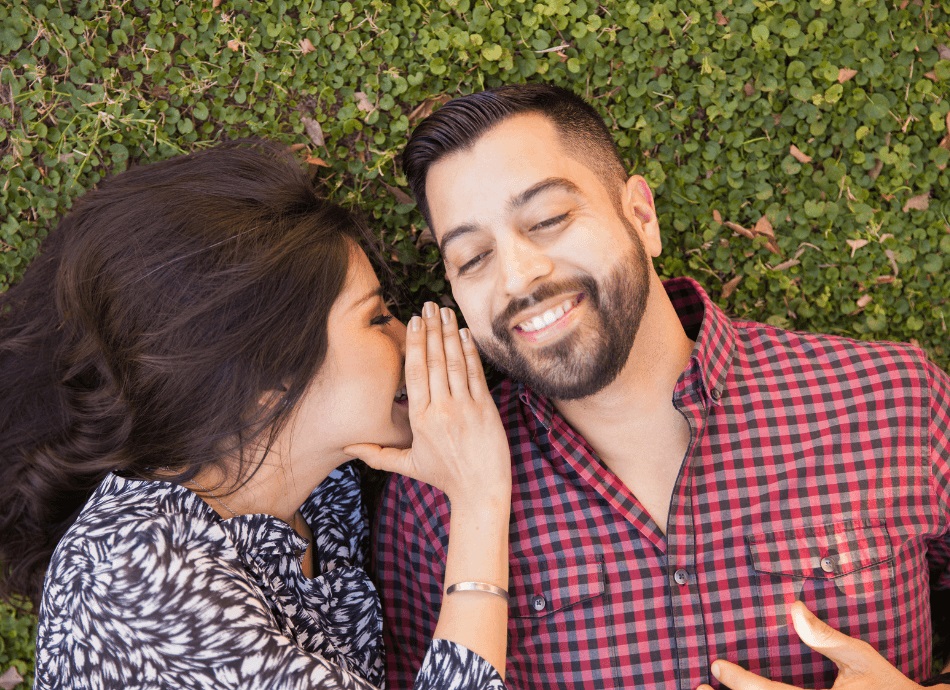 Woman whispering to partner lying on the grass