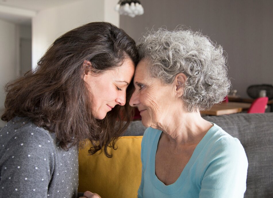 Adult daughter and mother touch foreheads supporting one another