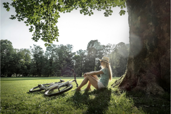 Woman wearing sunhat and glasses and sitting under tree 