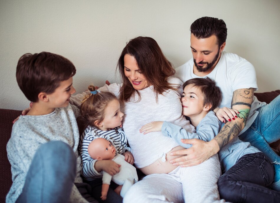 Large family of 5 hugging with pregnant mum on couch