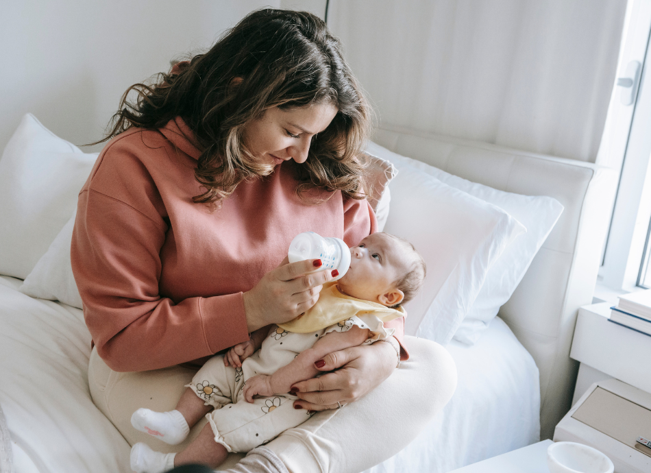 Woman sitting on bed bottle-feeding her baby