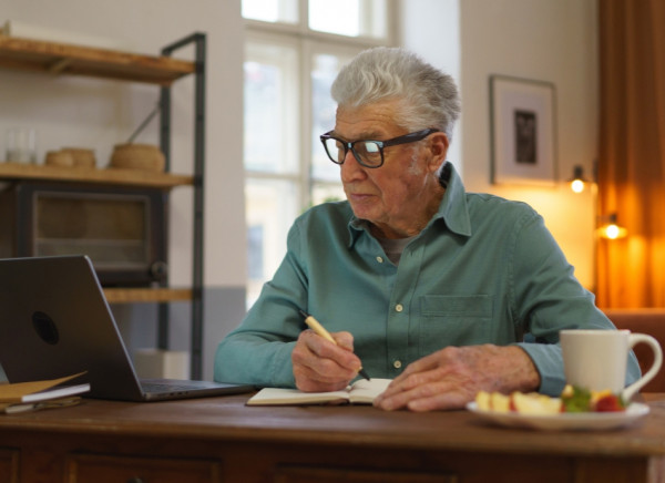 Older man sitting at computer taking notes in preparation for doctor's appointment