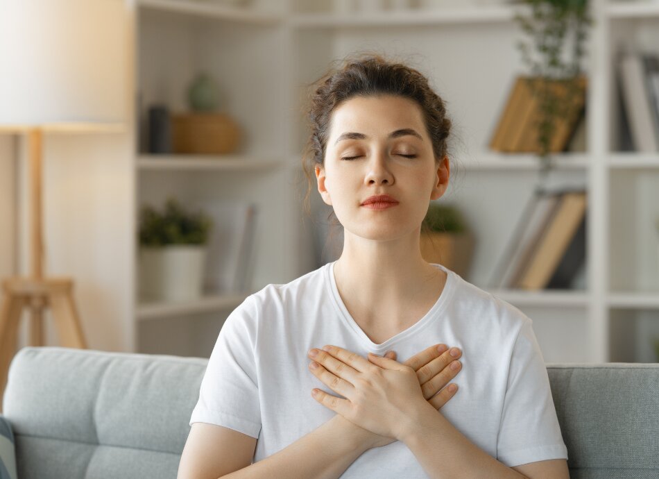 Woman sitting with hands across heart and eyes closed canva 950x690