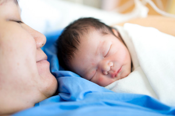 Mother smiling down at baby sleeping on her chest