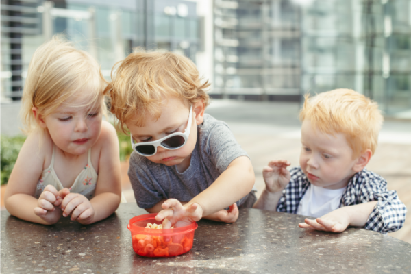 3 kids eating snacks from plastic container