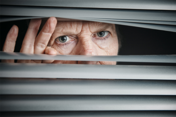 older woman looking through slats in a blind