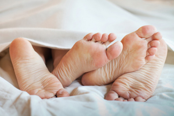 Two sets of feet entwined under bed sheets