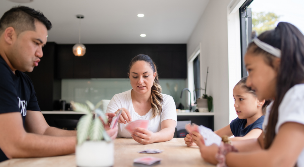 Whanau playing cards around table 