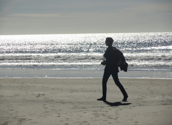 Woman silhouetted walking on beach in NZ